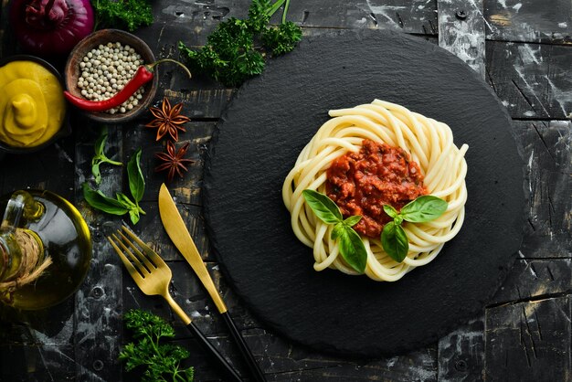 Spaghetti pasta with bolognese sauce and basil in a black stone plate Italian food Top view Free space for text