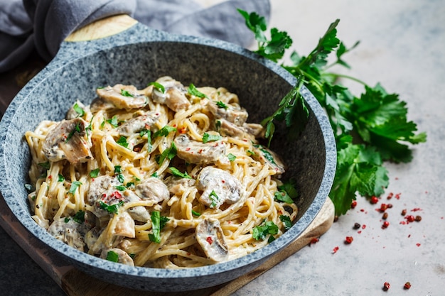 Spaghetti pasta with creamy sauce, mushrooms and parsley in a gray pan, gray background.