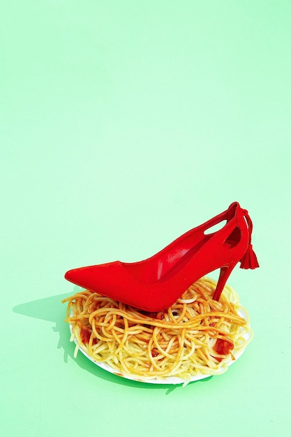 Spaghetti pasta with ketchup and red lady shoes on green background