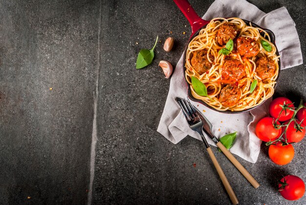 Spaghetti pasta with meatballs, basil tomato sauce in red cast iron pan, on black stone table 