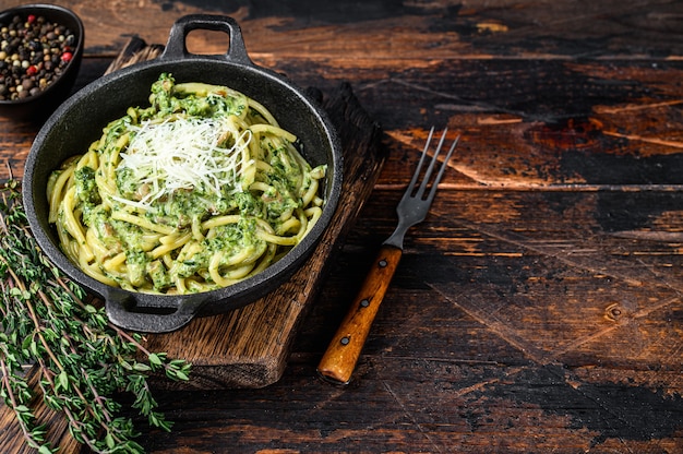 鍋にペストソース、ほうれん草、パルメザンチーズを入れたスパゲッティパスタ。暗い木の背景。上面図。スペースをコピーします。