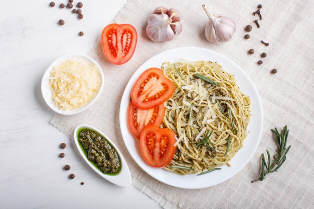 Spaghetti pasta with pesto sauce, tomatoes and cheese on a linen tablecloth