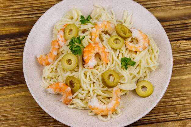 Spaghetti pasta with prawns green olives and parsley on wooden table Top view