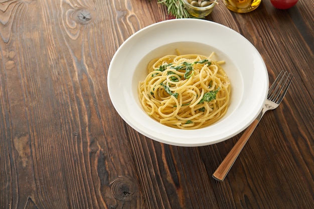 Spaghetti pasta with spinach leaves and cheese on a white plate on wooden table