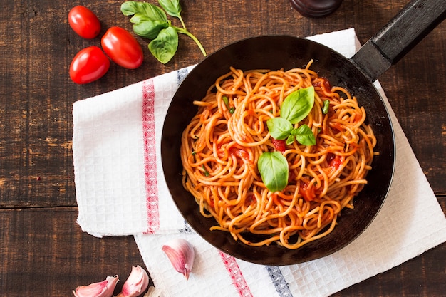 Spaghetti with basil leaf in frying pan on wooden table with ingredients