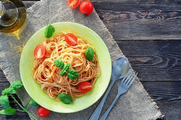 Spaghetti with fresh tomatoes and basil in a green plate on a rustic wooden table