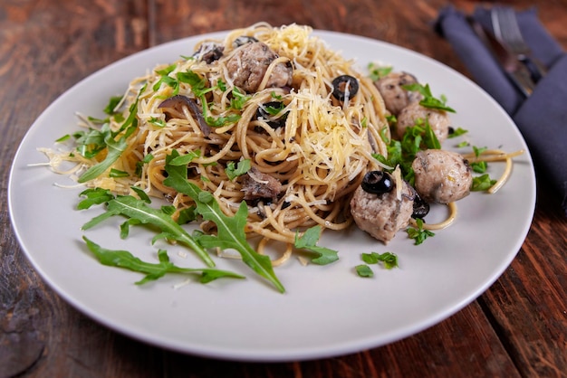 Spaghetti with meatballs olives and arugula on wood table