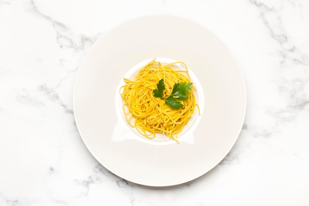 Spaghetti with parsley leaves in a white plate on a marble kitchen countertop