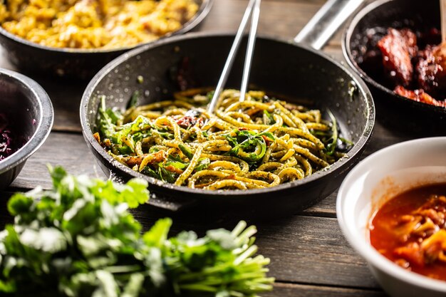 Spaghetti with pesto and parmesan cheese in a dark pan with tweezers in it.