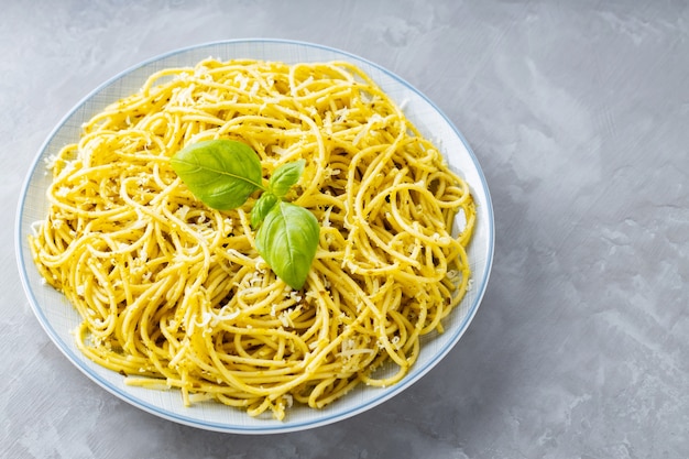 Spaghetti with pesto sauce and grated parmesan cheese on a gray background. Italian pasta with sauce pesto and basil leaves on a white plate. Copy space. Top view