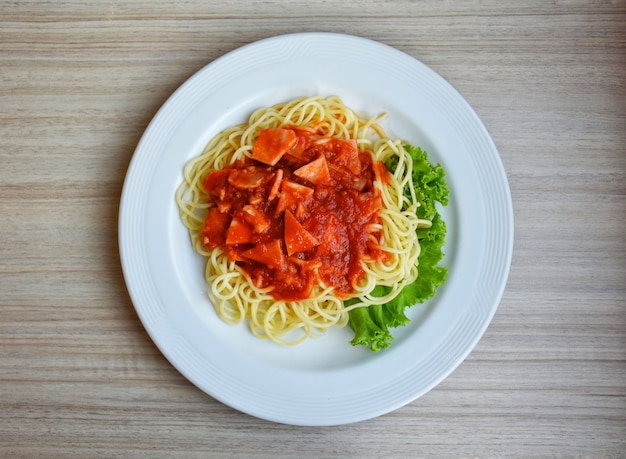 Foto spaghetti con salsa di pomodoro di maiale e foglie di verdure su sfondo bianco