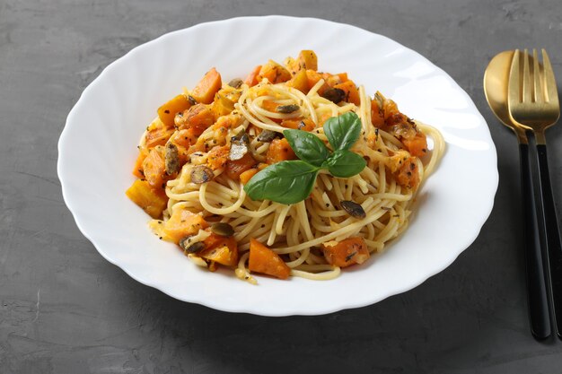 Spaghetti with pumpkin and pumpkin seeds in a white plate on a dark gray surface. Closeup
