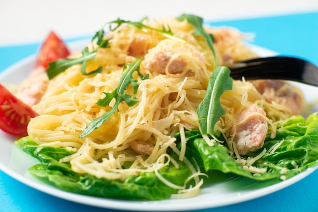 Spaghetti with salmon cheese on a lettuce salad sprinkled with arugula and cherry tomatoes closeup