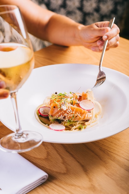 Foto la ragazza degli spaghetti al salmone mangia con un bicchiere di vino bianco