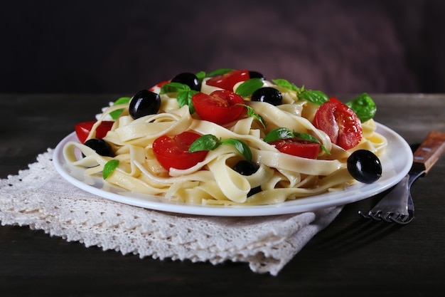 토마토 올리브와 바질 잎을 곁들인 스파게티는 벽 배경의 테이블에 있는 냅킨에 접시에 올려 놓습니다.
