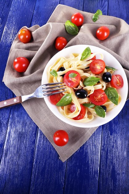 Spaghetti with tomatoes olives and basil leaves on plate on napkin on wooden background