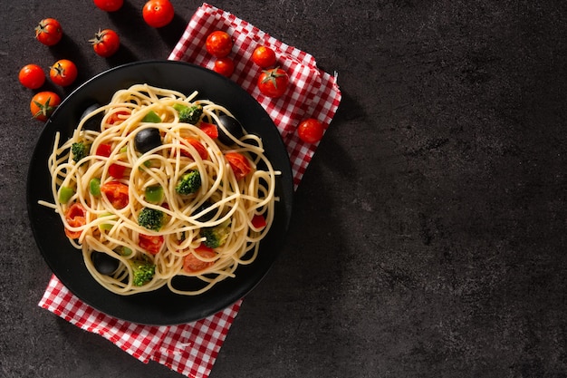 Spaghetti with vegetablesbroccolitomatoespeppers on black slate background