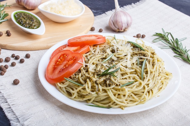 Spaghettideegwaren met pestosaus, tomaten en kaas op een linnentafelkleed op zwarte