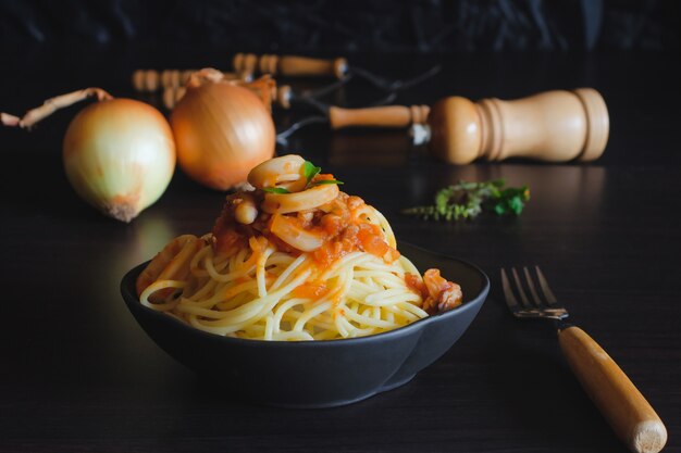 Spaghettideegwaren met tomatensaus en basilicum op plaat op donkere lijst.