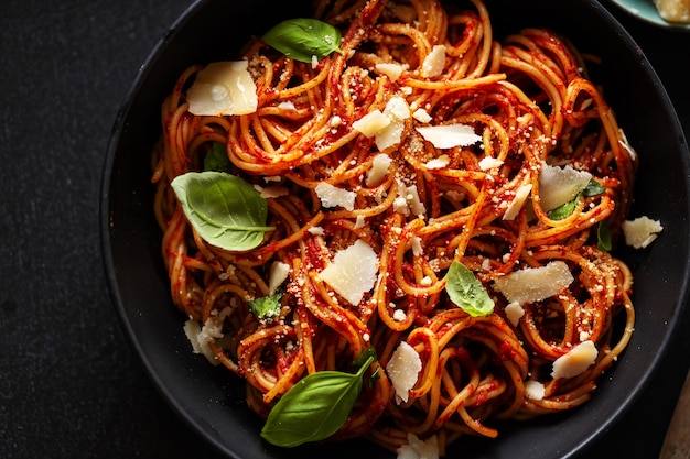 Spaghettideegwaren met tomatensaus, kaas en basilicum die in kom wordt gediend