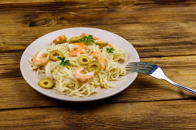 Spaghettipasta met garnalen, groene olijven en peterselie op houten tafel