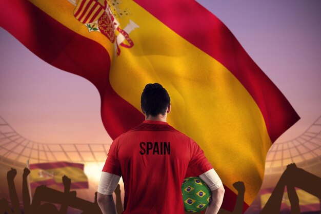 Фото Футболист испании держит мяч против большого футбольного стадиона под фиолетовым небом