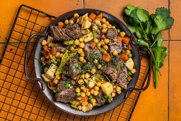 Spanish cocido Madrid stew with chickpeas meat carrots and potatoes Orange background Top view