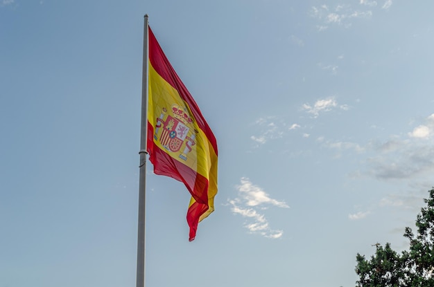 雲の青い空の背景で風に振られるスペインの旗