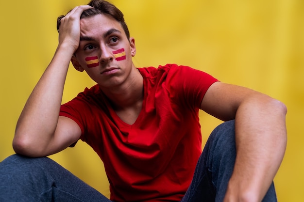 Spanish football fan sad for his national team isolated on yellow background Flag painted