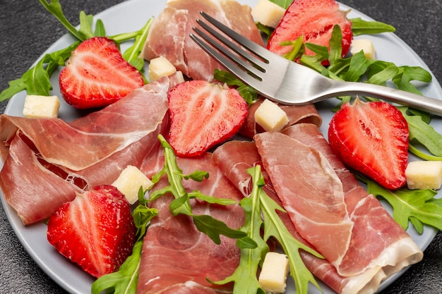 Spanish jamon with strawberries and arugula on gray plate