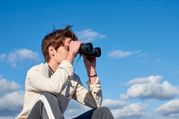 Spanish man in a beige shirt looking through binoculars on cloudy sky