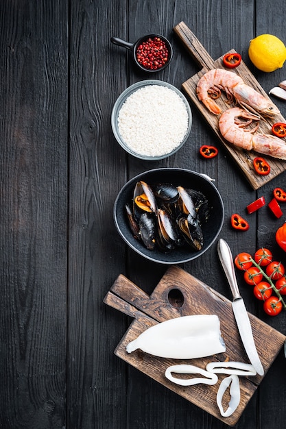 Ingredienti della paella spagnola con riso, gamberi, seppie e cozze su un tavolo di legno nero, vista dall'alto con spazio per il testo, foto di cibo.