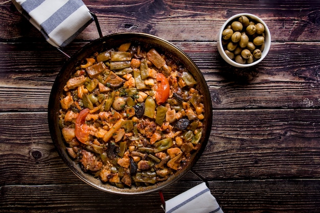 Spanish paella on a wooden table with green olives Traditional food