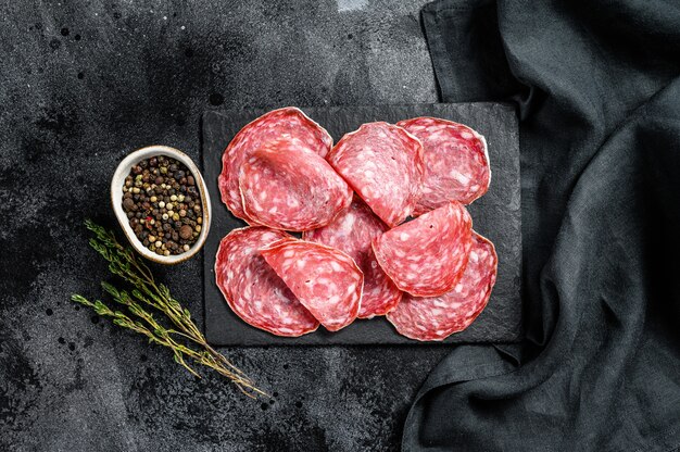 Spanish salami salchichon on a black chopping Board. Black background.