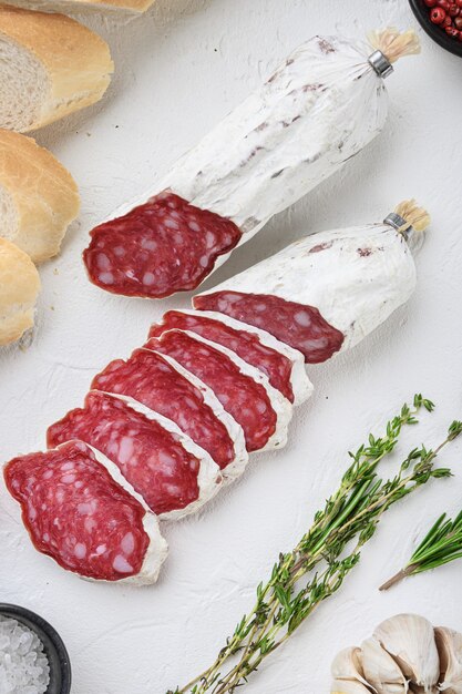 Spanish salcichon slices with panini and herbs on white surface, top view.