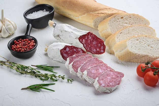 Spanish salcichon slices with panini and herbs on white surface.