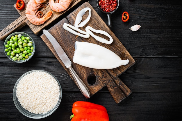 Spanish seafood paella ingredients, rice,prawns, mussels, peas over black wood table, flat lay with copy space