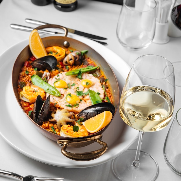 Spanish seafood paella in a pan with glass of wine