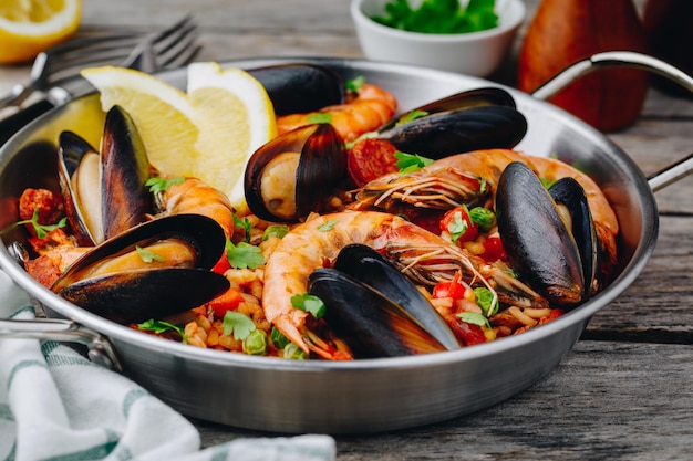 Spanish seafood paella with mussels shrimps and chorizo sausages in traditional pan on wooden background