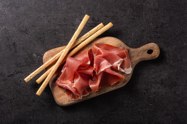 spanish serrano ham with breadstick on black background