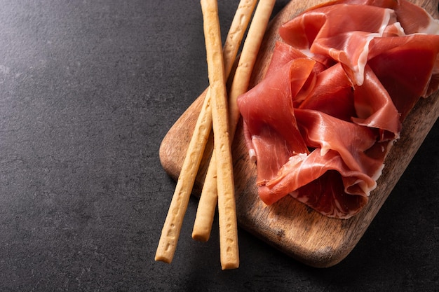 Spanish serrano ham with olives and breadstick on black background