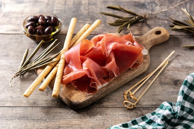 Spanish serrano ham with olives and breadstick on wooden table background