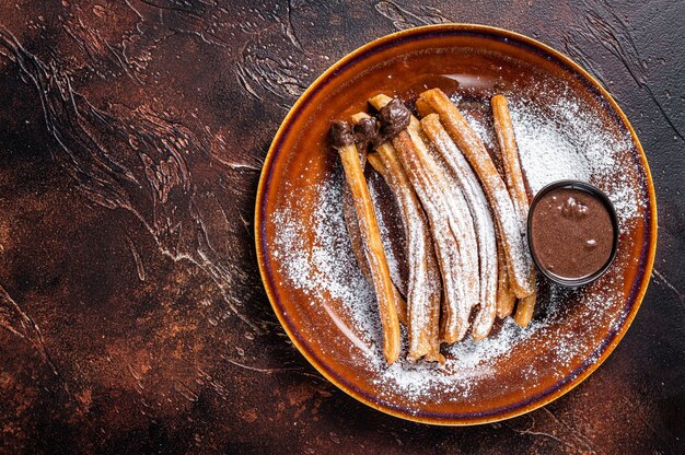 Spanish tapas churros with sugar and chocolate sauce. Dark background. Top view. Copy space.