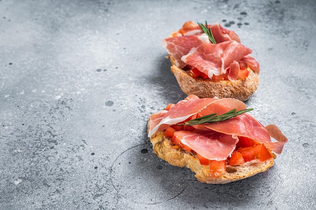 Spanish Tapas with tomatoes and cured Slices of jamon iberico ham fresh toasts Gray background Top view Copy space