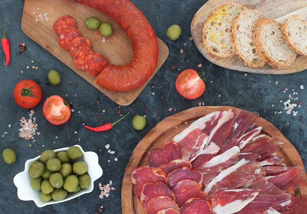 Spanish traditional chorizo sausage and ham on wooden cutboards and black concrete 