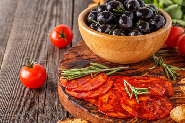 Spanish traditional chorizo sausage with fresh herbs, olives, tomatoes on a wooden board