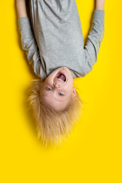 Spannende blonde jongen die ondersteboven op gele achtergrond hangt