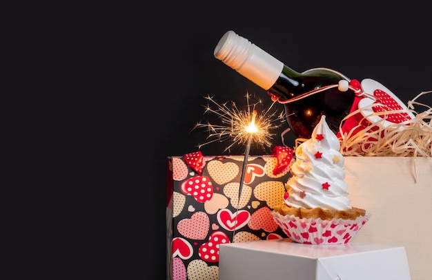 Sparkler, wine bottle, shopping bag with hearts and meringue cake on the black background for Valentine's day.