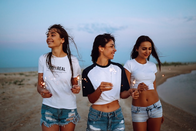 Photo the sparklers in the hands of young girls on the beach. three girls enjoying party on beach with sparklers. summer holidays, vacation, relax and lifestyle concept.