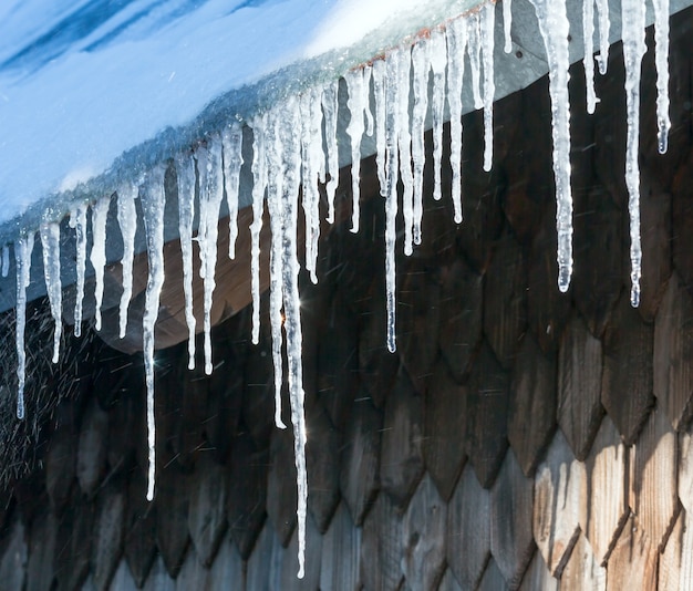 Foto scintillanti al sole lunghi ghiaccioli trasparenti che pendono dal tetto della casa.